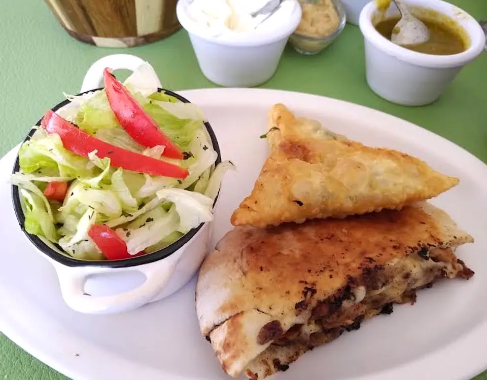 Empanada tipo fatayer dorada sobre un camello abierto relleno de carne y queso, con ensalada árabe