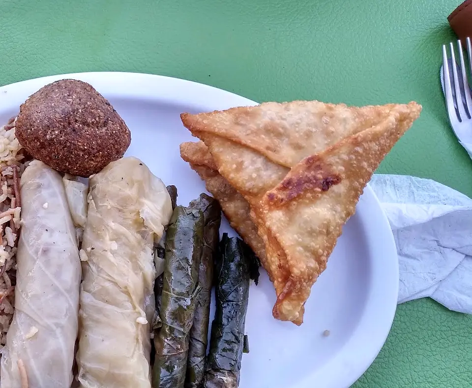 Dos empanadas tipo fatayer en triángulo junto a hojas de parra, repollos y un kipe bola, sobre la mesa verde de Saha