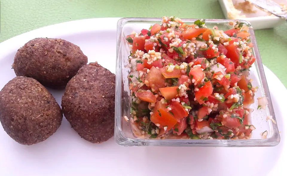 Tres kipe bola junto a un tazón de tapule con tomate, perejil y trigo